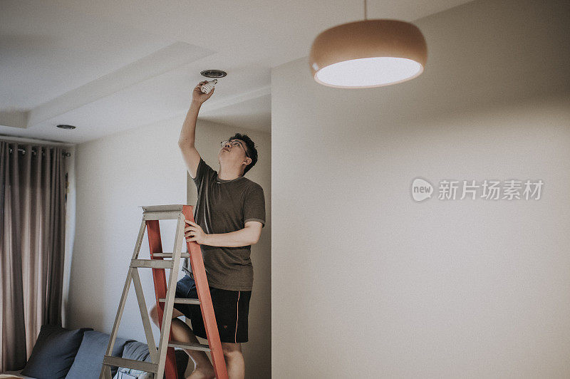 an asian chinese mid adult male changing light bulb in living room, apartment home